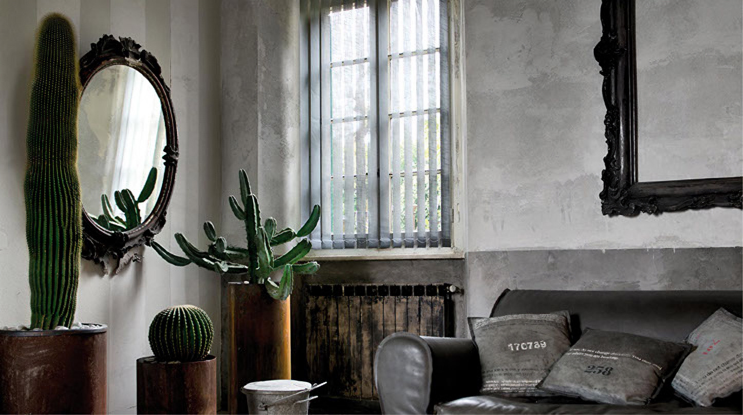 Grey vertical blinds at a tall window in a room with cacti, ornate mirrors and a leather sofa