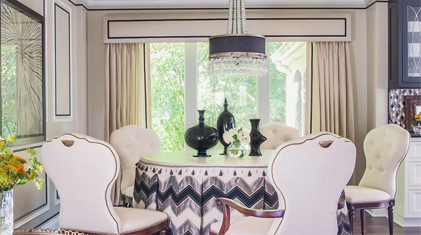 Dining room with cream curtains under a tailored valance, and a round table skirted in black and white chevron fabric